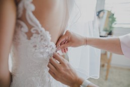 Die Schwester der Braut einer Weingut-Hochzeit schließt die letzten Knöpfe des Brautkleides fotografiert von Würzburger Hochzeitsfotografin Conny Schöffmann Photography