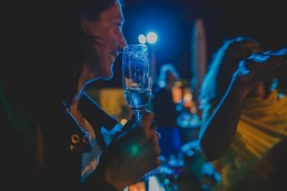 Strahlender Gast mit Sektglas in der Hand beobachtet die Tanzfläche einer Stadtstrandhochzeit unter freiem Himmel fotografiert von Hochzeitsfotografin Conny Schöffmann Photography aus Würzburg