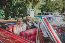 Glückliches Brautpaar sitzt in ihrem rotem Oldtimerhochzeitsauto fotografiert von Hochzeitsfotografin Conny Schöffmann Photography, Würzburg