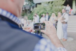 Enspannter Gast filmt das Brautpaar unter freiem Himmel fotografiert von Hochzeitsfotografin Conny Schöffmann Photography, Würzburg