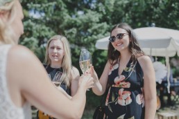 Lockeres Anstoßen der Braut mit einem Gast unter freiem Himmel auf einer Ruinenhochzeit fotografiert von Hochzeitsfotografin Conny Schöffmann Photography, Würzburg