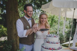 Brautpaar schneidet stimmungsvoll die Hochzeitstorte unter freiem Himmel an fotografiert von Würzburger Hochzeitsfotografin Conny Schöffmann Photography